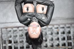 Dark-haired Asian hangs upside down in leather straitjacket